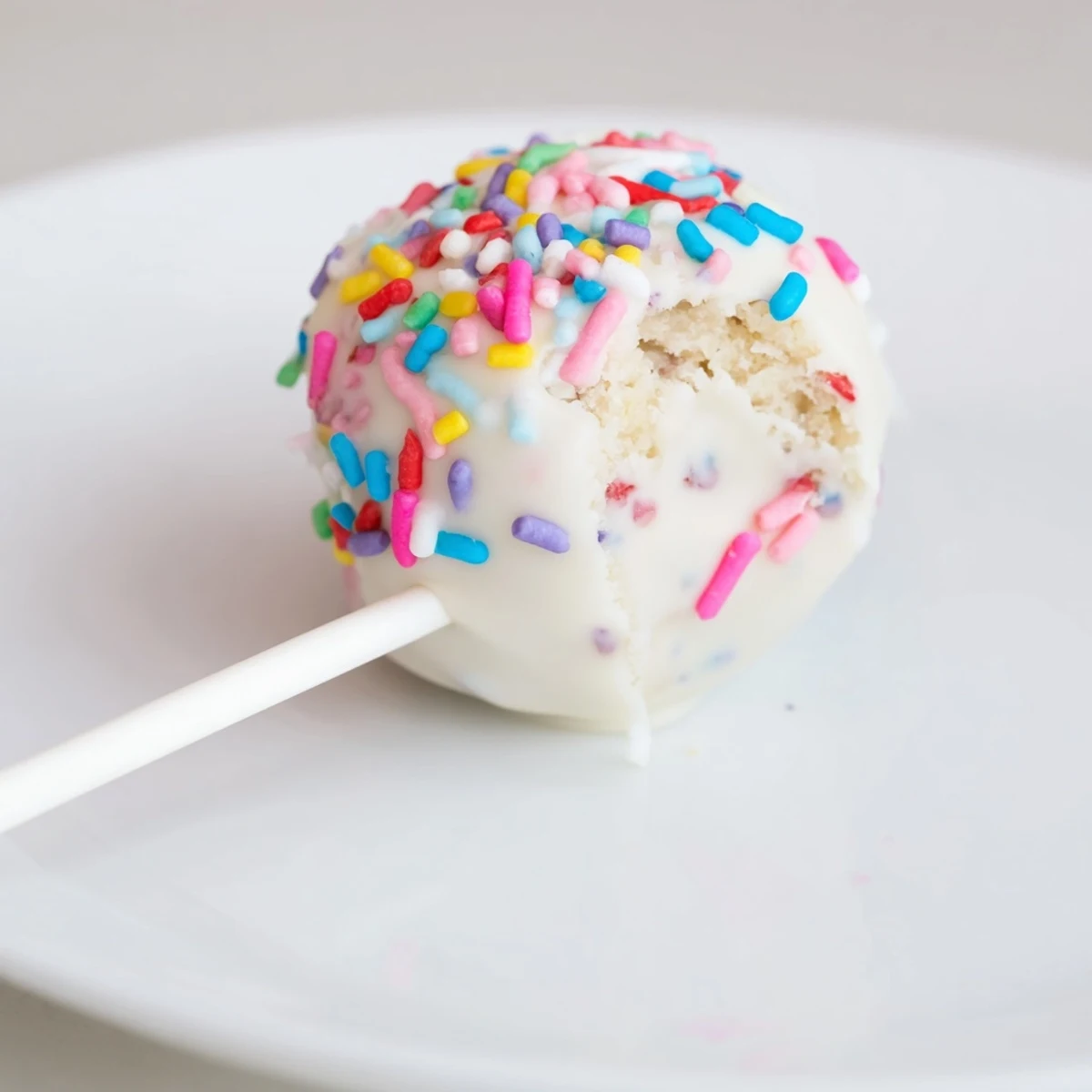 A close-up of a dreamy Lightened-Up Sugar Cookie Cake Pop, showing its creamy chocolate coating and colorful sprinkles.