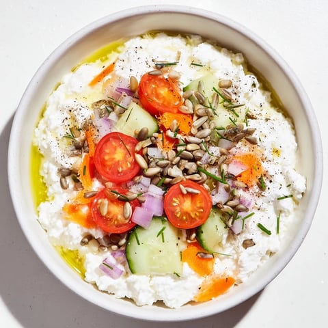 Creamy cottage cheese snack bowl with fresh veggies, olive oil and crunchy sunflower seeds.