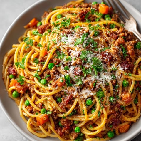 Hearty Spaghetti Bolognese with smoky bacon and peas served on a rustic white plate.