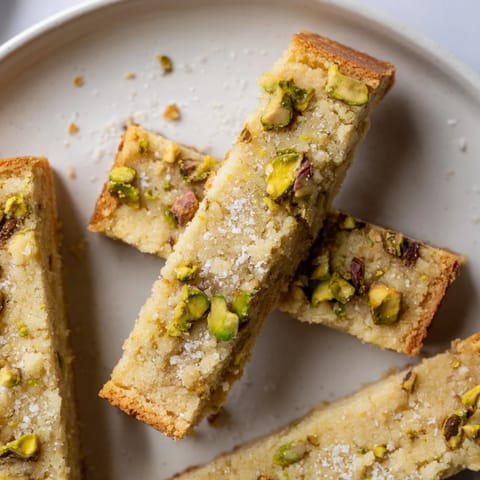 Close-up of golden Salted Pistachio Shortbread cookies, showing crunchy pistachios and sea salt topping.