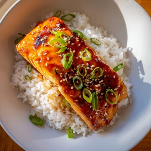 Vibrant image of Sticky Orange Salmon with glistening glaze atop a bed of buttery rice, garnished with greens.