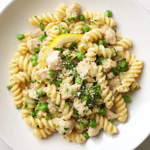 A close-up of tender chicken and peas in a creamy garlic butter sauce, served over curly pasta for a comforting dinner.